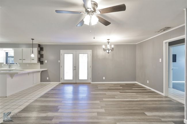 Unfurnished living room featuring french doors, ceiling fan with notable chandelier, light hardwood / wood-style flooring, and ornamental molding | Image 10