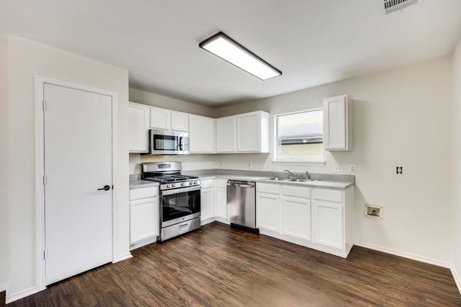 Kitchen with stainless steel appliances, light countertops, dark wood finished floors, white cabinets, and a sink | Image 12