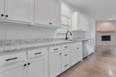 Kitchen with dishwasher, sink, a large fireplace, and white cabinets | Image 1