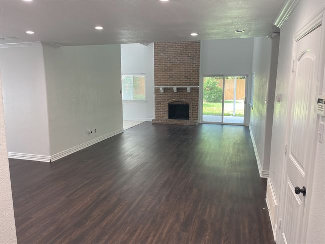 Unfurnished living room with plenty of natural light, dark wood finished floors, recessed lighting, a fireplace, and crown molding | Image 7