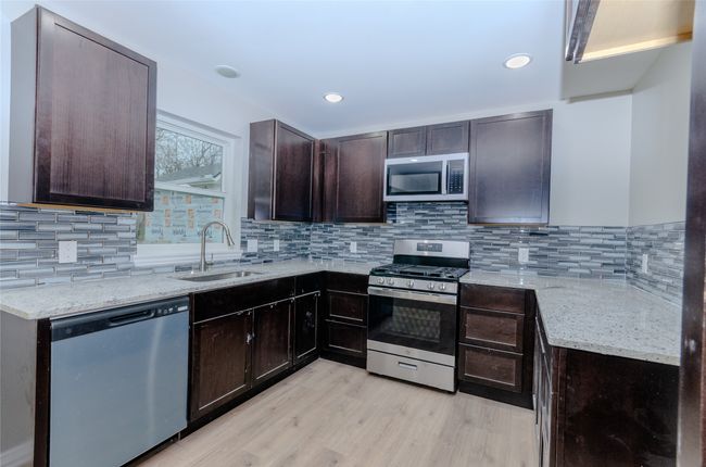 Kitchen featuring light stone countertops, stainless steel appliances, light wood-style floors, and a sink | Image 4
