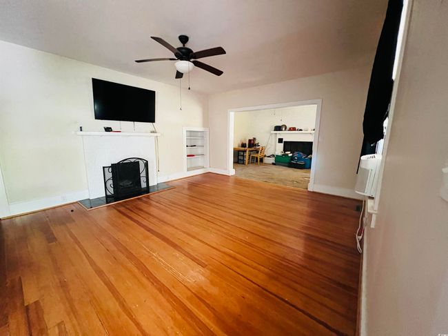 Unfurnished living room with a ceiling fan, baseboards, wood finished floors, and a fireplace | Image 5