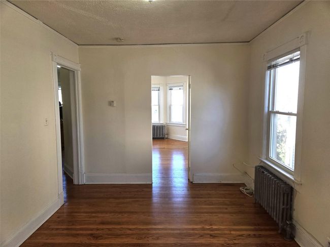 Empty room featuring radiator, plenty of natural light, wood finished floors, and a textured ceiling | Image 9