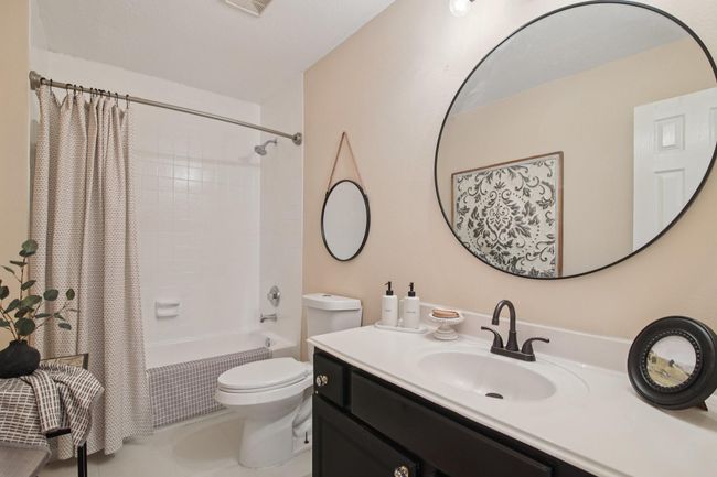 This bathroom features a clean design with a large round mirror above a white vanity. It includes a shower-tub combo , neutral wall colors, and decorative accents for a modern, inviting feel. | Image 24