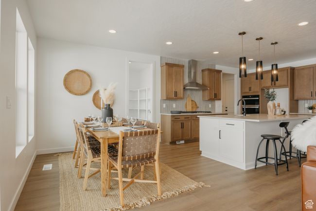 Kitchen with wall chimney range hood, decorative backsplash, light wood-style flooring, double wall oven, and a kitchen bar | Image 16