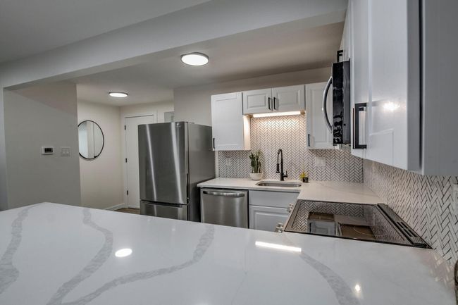 Kitchen with light stone counters, decorative backsplash, white cabinets, a sink, and appliances with stainless steel finishes | Image 16