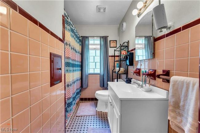 Bathroom with tile walls, toilet, vanity, a wainscoted wall, and a shower with curtain | Image 19