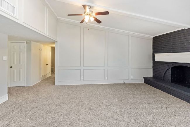 Unfurnished living room featuring carpet floors, a ceiling fan, a brick fireplace, a decorative wall, and visible vents | Image 13