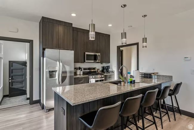 Kitchen with stainless steel appliances, a breakfast bar, light wood-type flooring, and a peninsula | Image 67