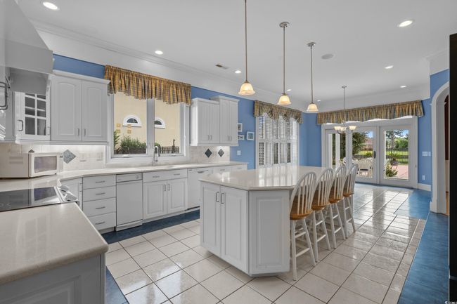 Kitchen with white appliances, a center island, backsplash, a kitchen bar, and light countertops | Image 10