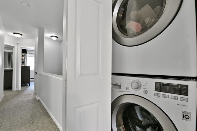Clothes washing area with light colored carpet, stacked washer / dryer, laundry area, and baseboards | Image 33