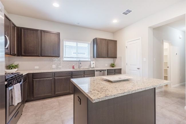 Kitchen featuring light stone counters, a sink, dark brown cabinetry, appliances with stainless steel finishes, and backsplash | Image 14