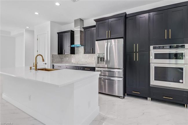 Kitchen featuring appliances with stainless steel finishes, a center island with sink, wall chimney range hood, sink, and backsplash | Image 20