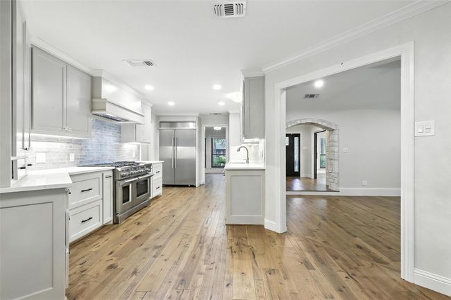 Kitchen with high quality appliances, arched walkways, light wood-type flooring, backsplash, and crown molding | Image 16