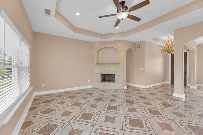 Unfurnished living room with arched walkways, a raised ceiling, a ceiling fan, a chandelier, and a fireplace | Image 8