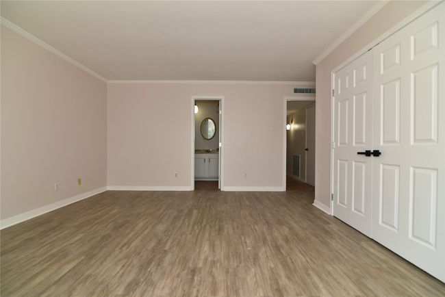Unfurnished bedroom with wood finished floors, crown molding, baseboards, connected bathroom, and a closet | Image 15