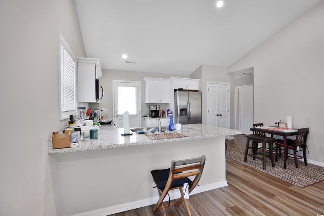 Kitchen featuring a peninsula, stainless steel appliances, white cabinets, vaulted ceiling, and light wood finished floors | Image 14