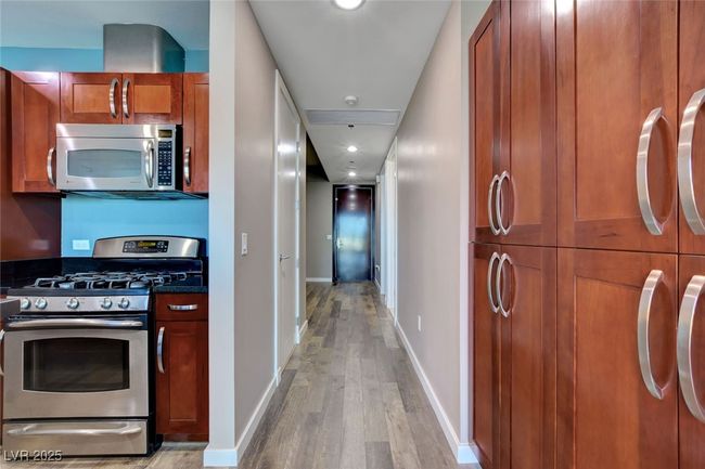 Kitchen with brown cabinets, dark countertops, baseboards, light wood-style flooring, and appliances with stainless steel finishes | Image 11