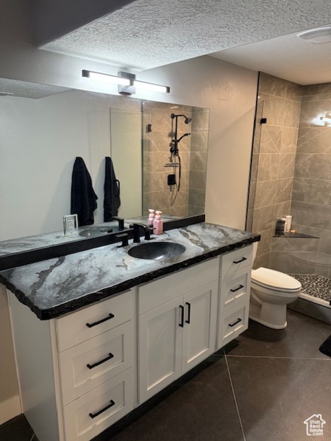 Bathroom featuring a stall shower, toilet, vanity, a textured ceiling, and tile patterned flooring | Image 17