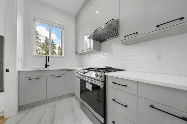 Kitchen featuring gas stove, under cabinet range hood, a sink, light marble finish floors, and light countertops | Image 4