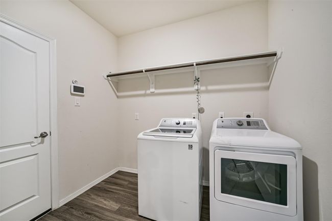 This spacious laundry room features a washer and dryer set, a shelf for storage, and a modern thermostat on the wall. The space has a clean, minimalist design with neutral walls and wood flooring. | Image 28