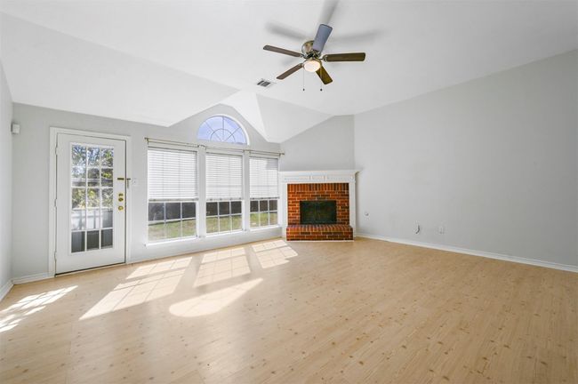 Unfurnished living room with lofted ceiling, wood finished floors, a brick fireplace, and a ceiling fan | Image 5