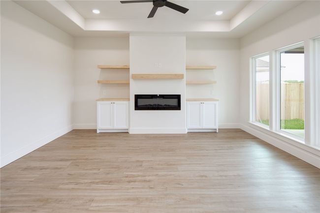 Unfurnished living room with a tray ceiling, a glass covered fireplace, light wood-type flooring, and recessed lighting | Image 6
