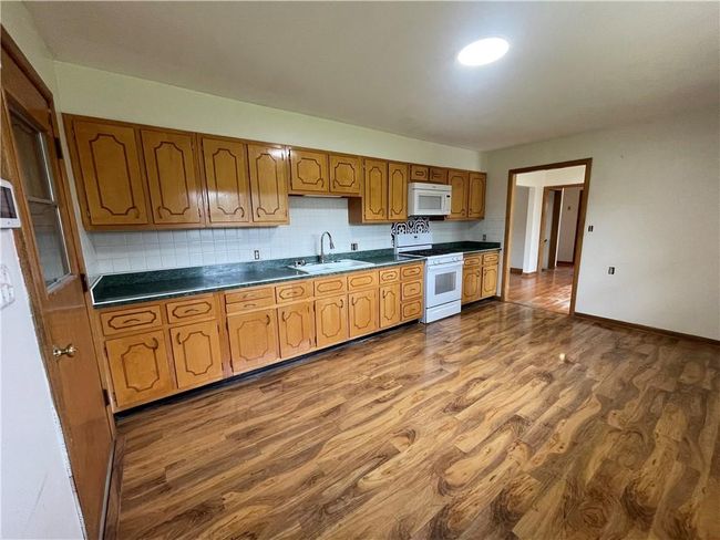 Kitchen with white appliances, dark countertops, backsplash, dark wood-style flooring, and a sink | Image 10