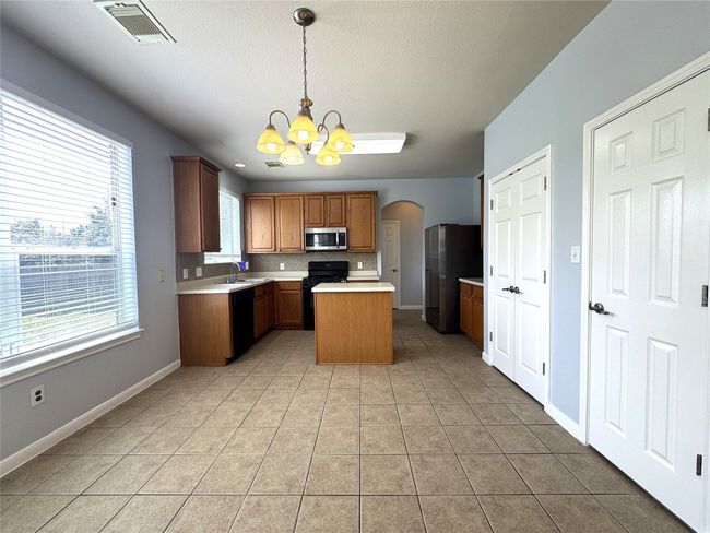 Kitchen featuring a chandelier, light tile patterned flooring, arched walkways, black appliances, and light countertops | Image 6