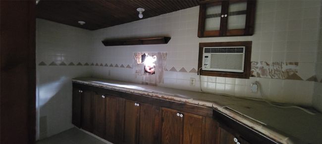 Laundry featuring light countertops, glass insert cabinets, tasteful backsplash, dark brown cabinets, and a wall mounted AC | Image 29
