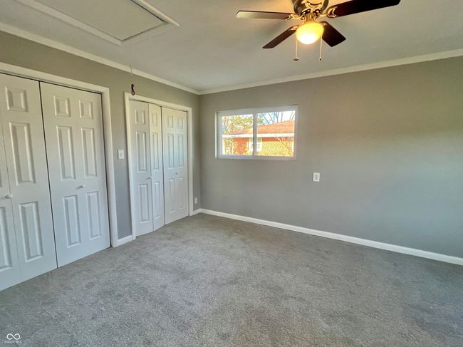 unfurnished bedroom with baseboards, attic access, two closets, crown molding, and carpet floors | Image 10