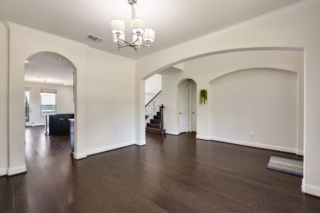 Empty room with a chandelier, dark wood-style floors, ornamental molding, stairs, and arched walkways | Image 9