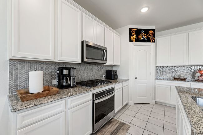 Kitchen featuring stainless steel appliances, light flooring, light granite counters, backsplash, and white cabinets | Image 16