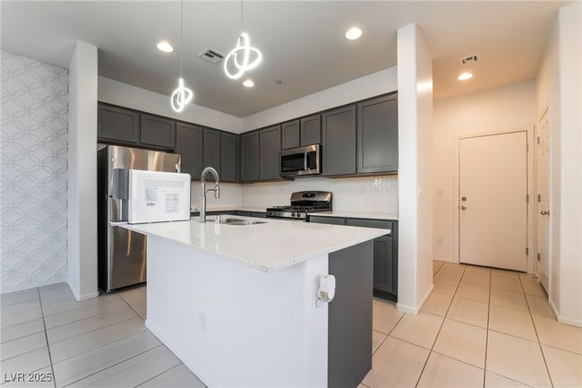 Kitchen featuring stainless steel appliances, light tile patterned floors, light stone countertops, decorative light fixtures, and an island with sink | Image 15