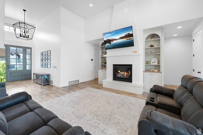 Living area featuring wood finished floors, a high ceiling, a chandelier, a glass covered fireplace, and built in features | Image 4