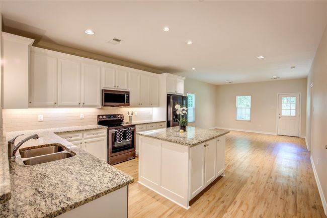 Kitchen with appliances with stainless steel finishes, a kitchen island, backsplash, light wood-type flooring, and white cabinets | Image 9