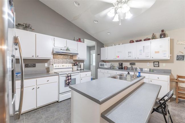 Kitchen with white appliances, a sink, under cabinet range hood, lofted ceiling, and a ceiling fan | Image 14