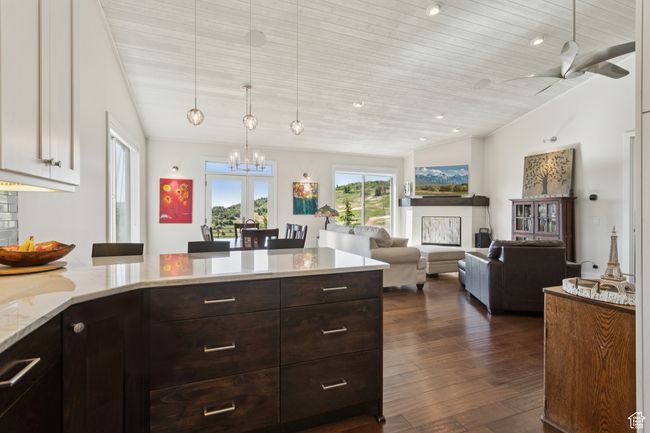 Kitchen with a chandelier, dark wood-type flooring, vaulted ceiling, dark brown cabinetry, and light stone countertops | Image 8