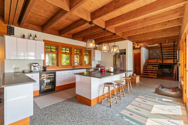 Kitchen with wine cooler, wood ceiling with exposed beams, appliances with stainless steel finishes, white cabinetry, and dark countertops | Image 5