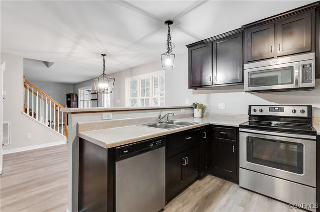 Kitchen with stainless steel appliances, a sink, light wood finished floors, a peninsula, and light countertops | Image 9