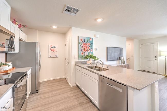 Kitchen featuring light wood-style floors, appliances with stainless steel finishes, white cabinets, a sink, and visible vents | Image 15