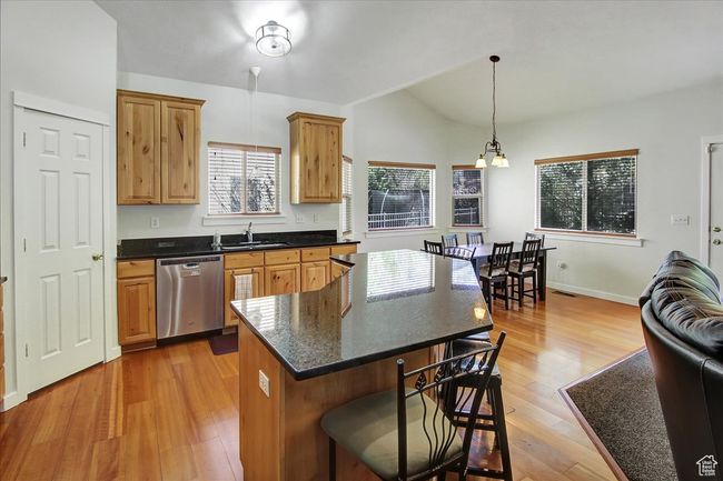 Kitchen with stainless steel dishwasher, a sink, light wood-style floors, lofted ceiling, and a breakfast bar area | Image 5