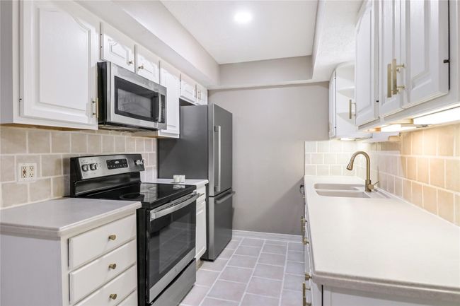 Kitchen featuring stainless steel appliances, a sink, white cabinets, light tile patterned flooring, and light countertops | Image 12