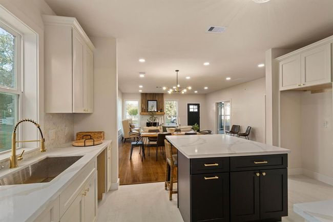 A stainless steel farmhouse sink, sitting just below a bright window, offers an elegant gold gooseneck faucet combining beauty with practicality. | Image 16