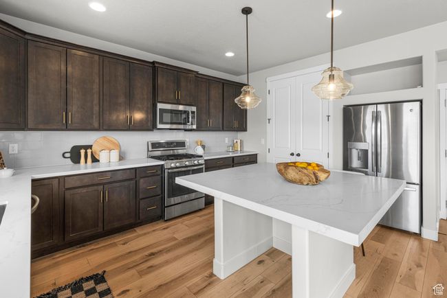 Kitchen featuring light wood finished floors, dark brown cabinetry, stainless steel appliances, and tasteful backsplash | Image 10
