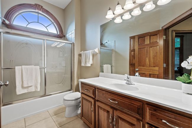 This second full bath on the main level features a tile bath/shower, expansive vanity surface, ceramic tile floors and a beautiful arched window to fill the space with natural light. | Image 23