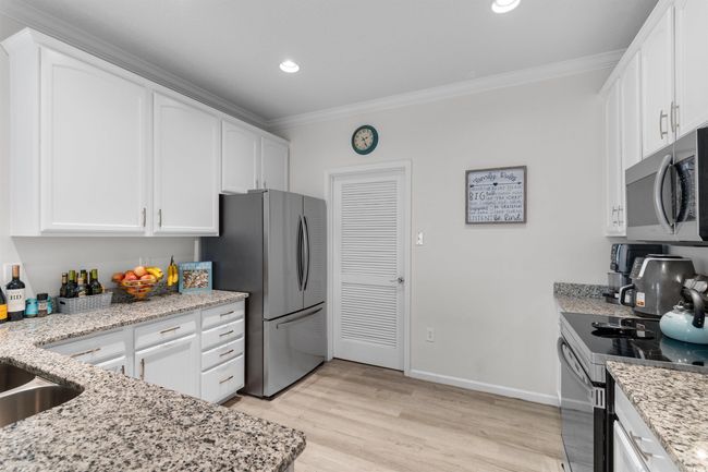 Kitchen with appliances with stainless steel finishes, crown molding, white cabinetry, light stone countertops, and light wood finished floors | Image 7