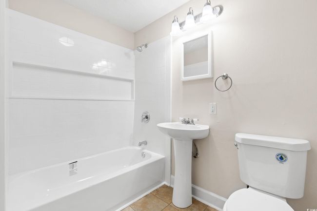 Bathroom with toilet, washtub / shower combination, tile patterned floors, and baseboards | Image 33