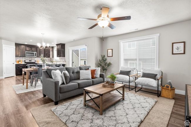 Living area with a chandelier, a ceiling fan, light wood-type flooring, baseboards, and a textured ceiling | Image 10