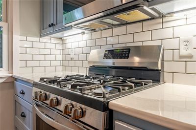 Kitchen with decorative backsplash, gray cabinetry, light stone countertops, and gas stove | Image 3